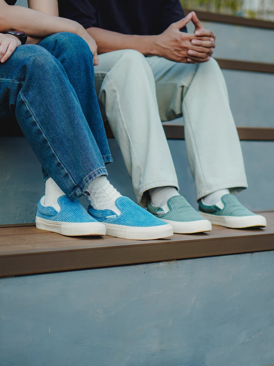 Two people seated on steps wearing blue and teal corduroy slip-ons
